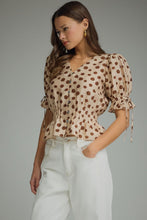 Polka dot V-neck short puff sleeve top featuring smocked waist. Button closure at front. Self-tie sleeve openings